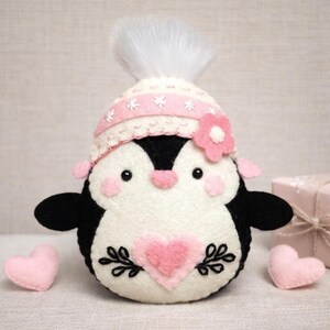 Valentine's Penguin felt ornament with pink hat, heart detail, and embroidery. DIY felt sewing pattern and SVG for Valentine's Day decor, love gifts, or easy craft projects. Perfect for beginners and experienced crafters to create a handmade decor