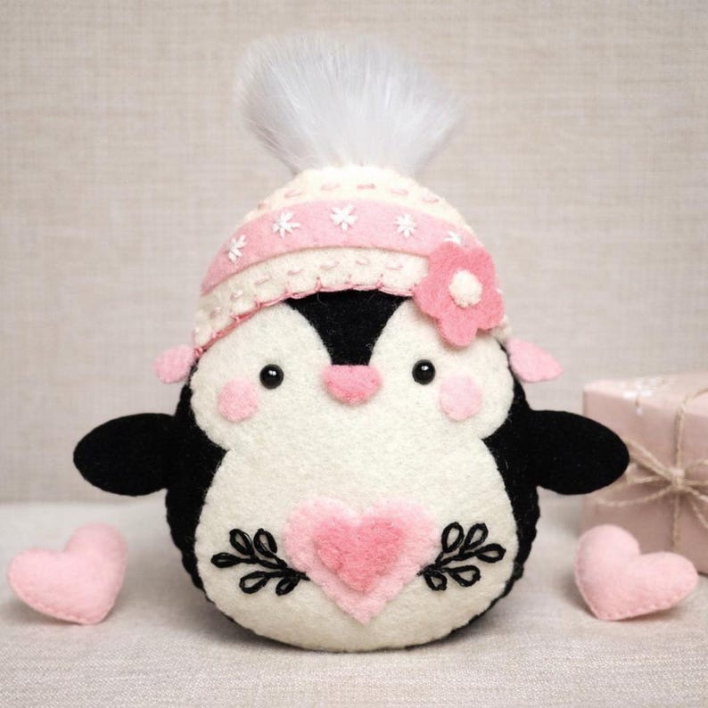 Valentine's Penguin felt ornament with pink hat, heart detail, and embroidery. DIY felt sewing pattern and SVG for Valentine's Day decor, love gifts, or easy craft projects. Perfect for beginners and experienced crafters to create a handmade decor