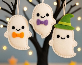 Puede incluir: Tres adornos de fantasmas de fieltro blanco colgados de cuerdas. Un fantasma lleva una pajarita naranja, otro una pajarita morada y el tercero un sombrero de bruja verde. Cada fantasma tiene ojos negros circulares y una pequeña sonrisa.