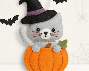 May include: A felt ornament featuring a gray cat wearing a black witch hat with a purple band, sitting inside an orange pumpkin. The cat has black bead eyes, a stitched nose, and pink cheeks. A small green leaf is attached to the pumpkin.