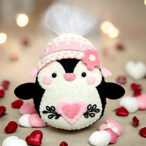 Valentine's or Christmas and winter Penguin felt ornament with pink hat, heart detail, and embroidery. DIY PDF felt sewing pattern and SVG for Valentine's Day decor, love gifts, or easy craft projects. Perfect for beginners and experienced crafters to create a handmade decor