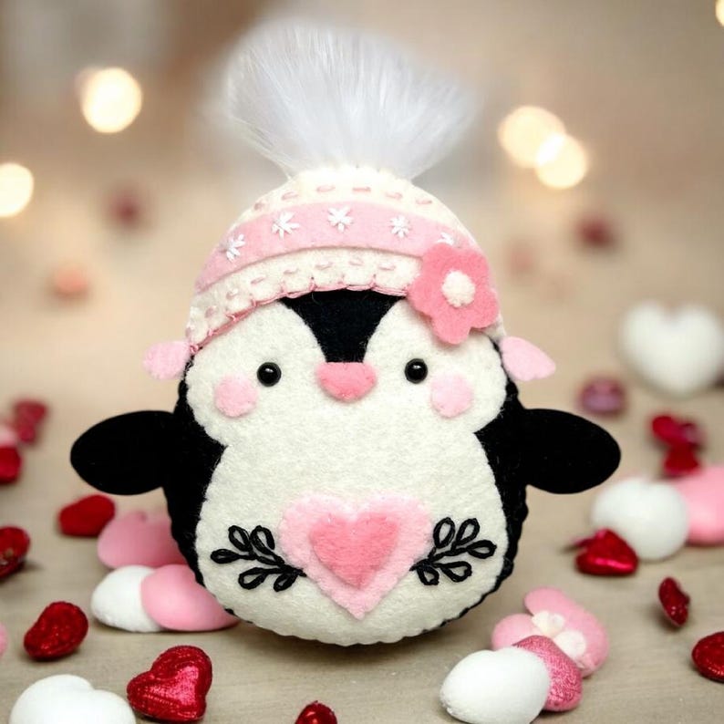 Valentine's or Christmas and winter Penguin felt ornament with pink hat, heart detail, and embroidery. DIY PDF felt sewing pattern and SVG for Valentine's Day decor, love gifts, or easy craft projects. Perfect for beginners and experienced crafters to create a handmade decor