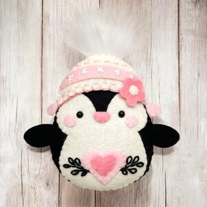 Valentine's Penguin felt ornament with pink hat, heart detail, and embroidery. DIY felt sewing pattern and SVG for Valentine's Day decor, love gifts, or easy craft projects. Perfect for beginners and experienced crafters to create a handmade decor