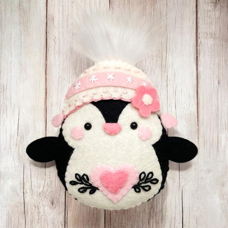Valentine's Penguin felt ornament with pink hat, heart detail, and embroidery. DIY felt sewing pattern and SVG for Valentine's Day decor, love gifts, or easy craft projects. Perfect for beginners and experienced crafters to create a handmade decor