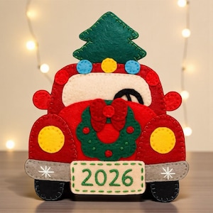 Puede incluir: Adorno navideño de coche rojo de fieltro con un árbol de Navidad verde de fieltro en la parte superior. El coche tiene faros amarillos, un parabrisas blanco y una matrícula que dice "2026". El coche está decorado con una corona verde y un lazo rojo.