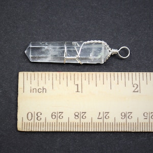 May include: A clear quartz crystal point wrapped in silver wire with a silver loop for hanging. The crystal is approximately 1 inch long.