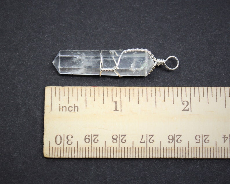 May include: A clear quartz crystal point wrapped in silver wire with a silver loop for hanging. The crystal is approximately 1 inch long.