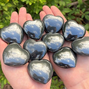 May include: A collection of ten polished black hematite heart-shaped stones. The stones are smooth and have a reflective surface.