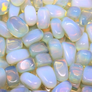 May include: A close-up of a pile of iridescent white opal tumbled stones. The stones are smooth and polished, with a milky white color and a rainbow sheen.