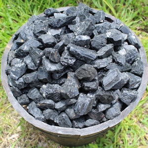 May include: A wooden bowl filled with black tourmaline rough crystals. The crystals are various sizes and shapes, with some having a pointed or elongated shape.