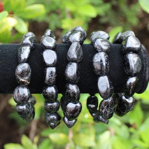 May include: Four bracelets made of polished, irregular black tourmaline stones. Each bracelet consists of smooth, rounded, dark, reflective mineral beads strung together, displaying natural variations in shape and size across the set.