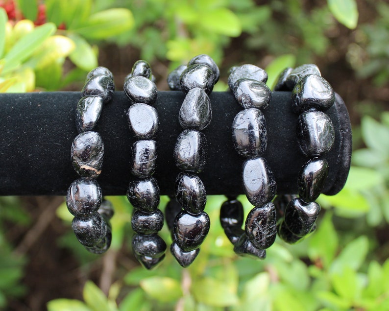 May include: Four bracelets made of polished, irregular black tourmaline stones. Each bracelet consists of smooth, rounded, dark, reflective mineral beads strung together, displaying natural variations in shape and size across the set.
