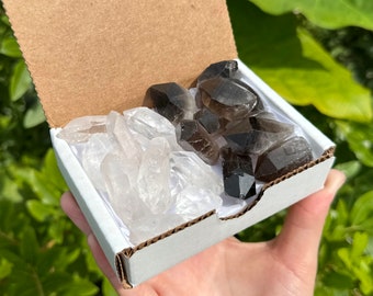 Puede incluir: Una caja blanca llena de cristales de cuarzo transparente y cristales de cuarzo ahumado. La caja está abierta y los cristales son visibles.