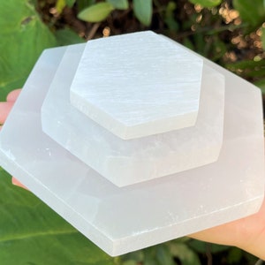 May include: Three white selenite charging plates stacked on top of each other. The plates are hexagonal in shape and have a smooth, polished surface.