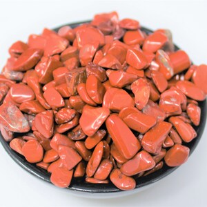 Puede incluir: Un cuenco lleno de piedras de jaspe rojo pulidas. Las piedras son lisas y pulidas, de un color rojo intenso.