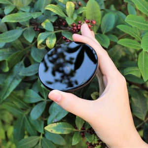 May include: A black round mirror with a reflective surface. The mirror is being held in a hand.