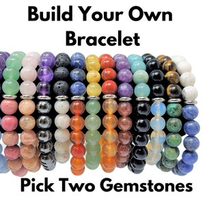 May include: A variety of gemstone bracelets in different colors, including green, pink, purple, black, blue, and yellow. The bracelets are stacked on top of each other and the text "Build Your Own Bracelet" and "Pick Two Gemstones" is visible at the top and bottom of the image.