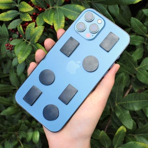 May include: A blue smartphone case with multiple black round and rectangular magnetic attachments. The case is being held in a hand.