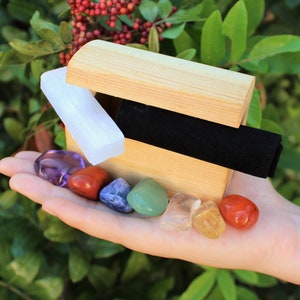 May include: A wooden box with a black velvet lining contains seven chakra stones: amethyst, carnelian, lapis lazuli, green aventurine, clear quartz, citrine, and red jasper.