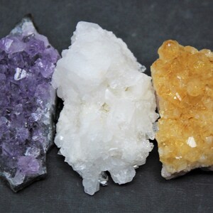 May include: Three clusters of crystals, one purple amethyst, one white quartz, and one yellow citrine.