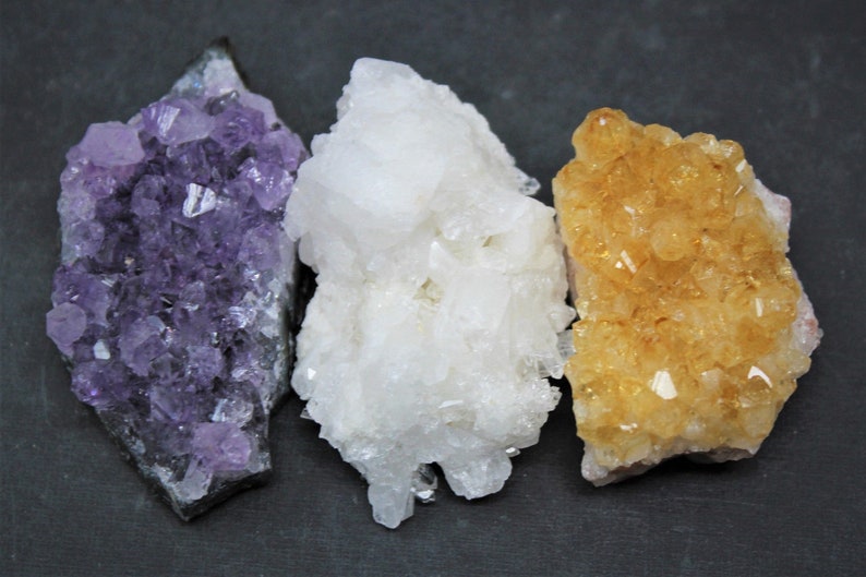 May include: Three clusters of crystals, one purple amethyst, one white quartz, and one yellow citrine.