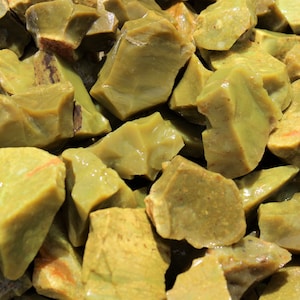 May include: A close-up of a pile of green and yellow opal rough. The rough is irregularly shaped and has a translucent appearance.