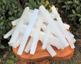 May include: A pile of white selenite sticks on a wooden surface. The sticks are smooth and have a natural, crystalline texture.