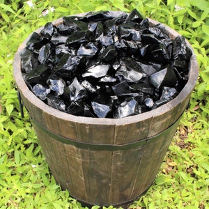 Puede incluir: Un barril de madera lleno de virutas de obsidiana negra. El barril est&aacute; sentado sobre un lecho de hierba verde.