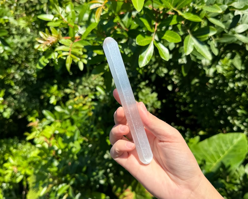 May include: A white selenite wand with a smooth, polished surface. The wand is about 10 inches long and has a slightly rounded end.