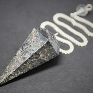May include: A black, faceted, pointed pendulum with a silver chain. The pendulum is used for divination and dowsing.