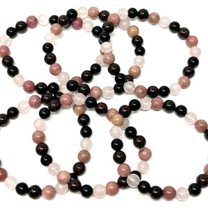 May include: Four bracelets made of black, pink, and white beads. The bracelets are made of natural stones and are stacked on top of each other.