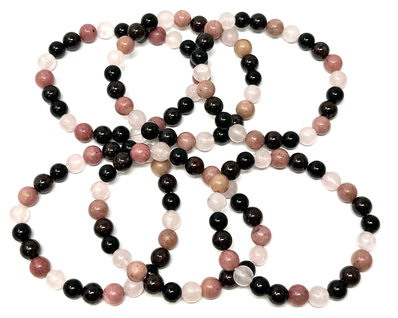 May include: Four bracelets made of black, pink, and white beads. The bracelets are made of natural stones and are stacked on top of each other.