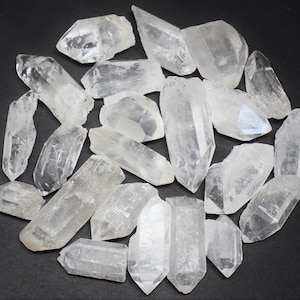 May include: A collection of clear quartz crystal points and chunks, varying in size and shape. The crystals are arranged in a circular pattern against a dark background, showcasing their natural, translucent appearance. These raw gemstones are ideal for crystal healing and metaphysical practices.