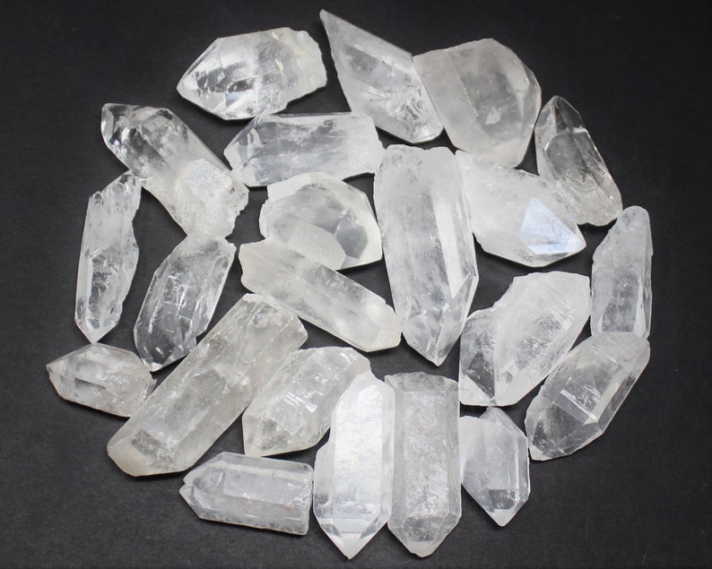 May include: A collection of clear quartz crystal points and chunks, varying in size and shape. The crystals are arranged in a circular pattern against a dark background, showcasing their natural, translucent appearance. These raw gemstones are ideal for crystal healing and metaphysical practices.