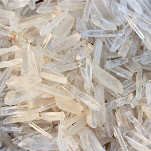 May include: A large pile of clear quartz crystal points. The points are of various sizes and shapes, and they are all very shiny.