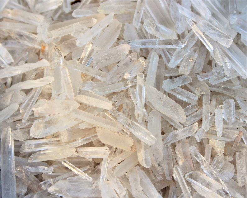 May include: A large pile of clear quartz crystal points. The points are of various sizes and shapes, and they are all very shiny.
