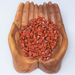 Puede incluir: Un cuenco de madera con forma de mano lleno de virutas de jaspe rojo. El cuenco est&aacute; hecho de madera natural y tiene un acabado r&uacute;stico.