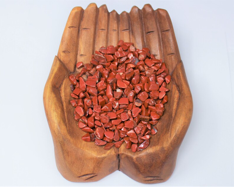 Puede incluir: Un cuenco de madera con forma de mano lleno de virutas de jaspe rojo. El cuenco est&aacute; hecho de madera natural y tiene un acabado r&uacute;stico.