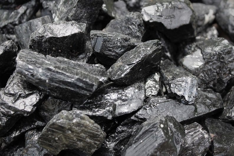 May include: A close-up of a pile of black tourmaline crystals. The crystals are rough and have a natural, unpolished look.