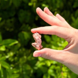 May include: A small, irregular copper nugget with a metallic, reddish-brown finish and a textured, uneven surface. The nugget displays a natural, raw appearance with various indentations and protrusions across its compact, solid form.