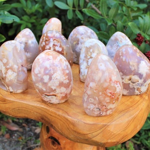 May include: A collection of ten white, pink, and orange agate freeform points with a white, flower-like pattern. The points are arranged on a wooden stand.
