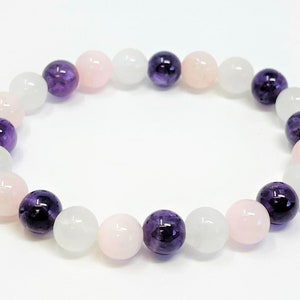 May include: A bracelet made with white, pink, and purple beads. The beads are round and smooth.