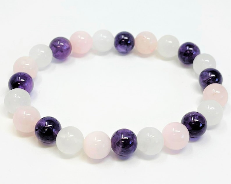 May include: A bracelet made with white, pink, and purple beads. The beads are round and smooth.