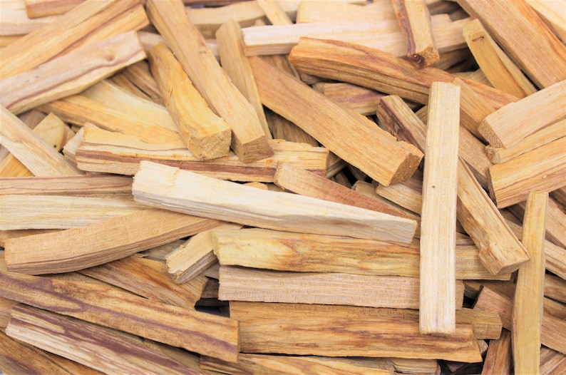 May include: A collection of light brown Palo Santo wood sticks. The sticks are rectangular, with varying shades of tan and brown. Some sticks have visible grain patterns and knots. The wood appears to be freshly cut.