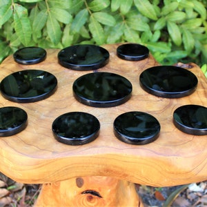 May include: Nine black obsidian coasters, round and polished, arranged on a wooden surface.
