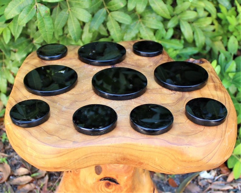 May include: Nine black obsidian coasters, round and polished, arranged on a wooden surface.
