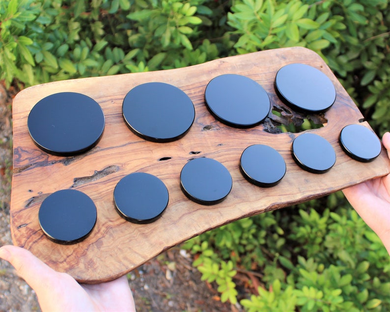 May include: A set of nine black round coasters on a wooden surface. The coasters are different sizes and are arranged in a semi-circle.