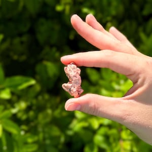 May include: A small, irregular copper nugget with a metallic, reddish-brown finish and a textured, uneven surface. The nugget displays a natural, raw appearance with various indentations and protrusions across its compact, solid form.