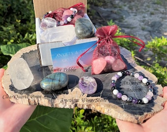 May include: A set of crystals for anxiety and stress relief. The set includes a clear quartz point, labradorite pebble, amethyst worry stone, and a tumbled stone kit with four pink stones. The set also includes a bracelet with amethyst, clear quartz, and black onyx beads.