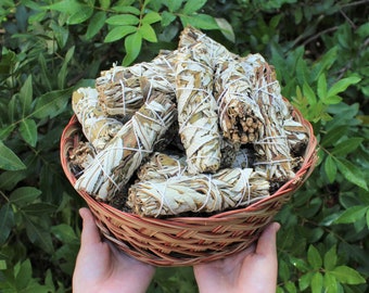 May include: A wicker basket filled with white sage smudge sticks. The sticks are tied with twine and have a natural, earthy look.